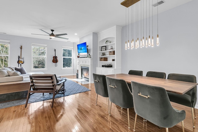 dining room featuring built in shelves, light wood-type flooring, and ceiling fan