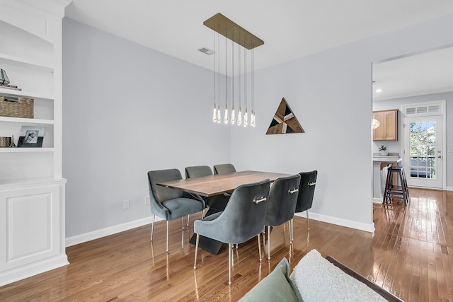 dining space with built in shelves and wood-type flooring