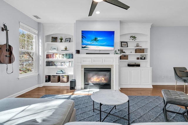 living room featuring built in shelves, dark hardwood / wood-style floors, and ceiling fan