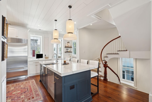 kitchen with a breakfast bar, sink, built in refrigerator, decorative light fixtures, and white cabinets