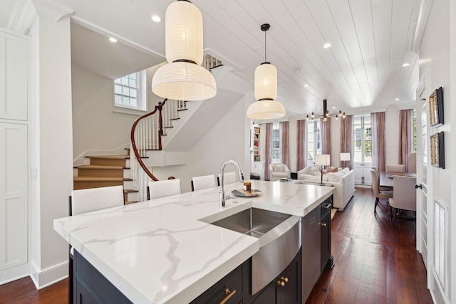 kitchen featuring pendant lighting, sink, dark hardwood / wood-style floors, light stone counters, and a center island with sink