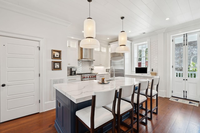 kitchen featuring white cabinetry, hanging light fixtures, high end appliances, light stone countertops, and wall chimney range hood