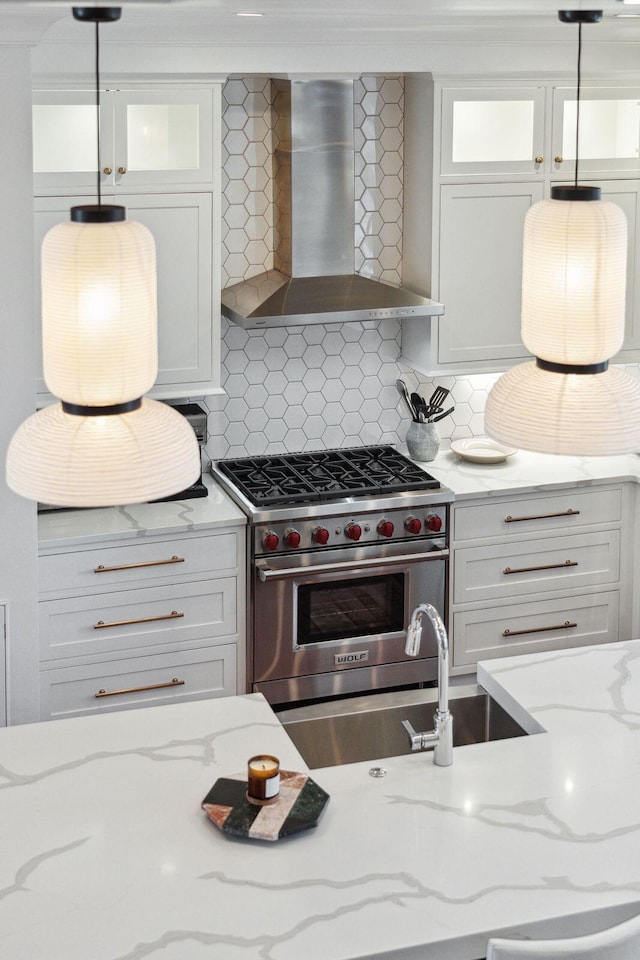 kitchen featuring white cabinets, designer stove, hanging light fixtures, and wall chimney range hood