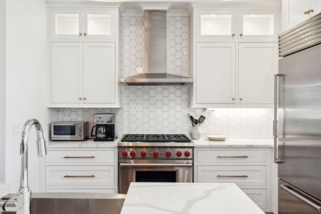 kitchen featuring wall chimney range hood, premium appliances, and white cabinets