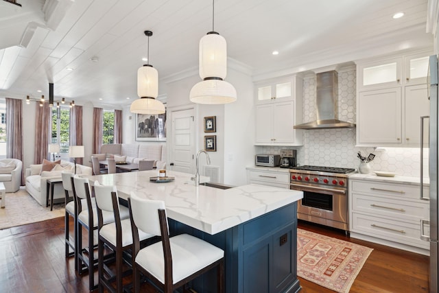 kitchen with premium range, light stone countertops, an island with sink, white cabinets, and wall chimney exhaust hood