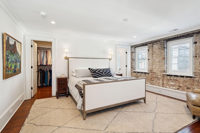 bedroom with hardwood / wood-style flooring, brick wall, and a spacious closet