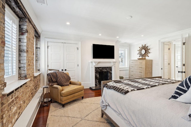 bedroom featuring hardwood / wood-style flooring, ornamental molding, a high end fireplace, and a closet