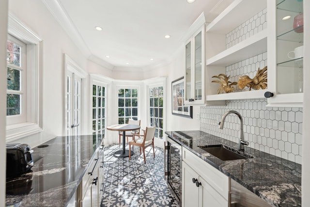 kitchen with sink, dark stone countertops, plenty of natural light, white cabinets, and beverage cooler