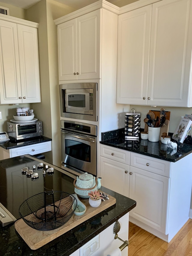 kitchen featuring appliances with stainless steel finishes, light hardwood / wood-style floors, white cabinets, and dark stone counters