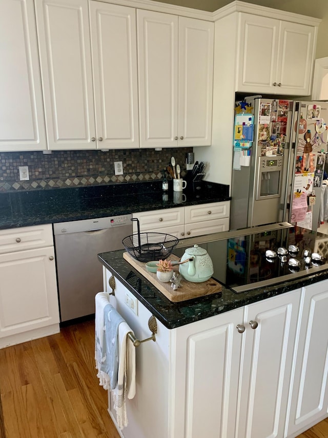 kitchen with stainless steel appliances, white cabinets, tasteful backsplash, light hardwood / wood-style floors, and dark stone counters