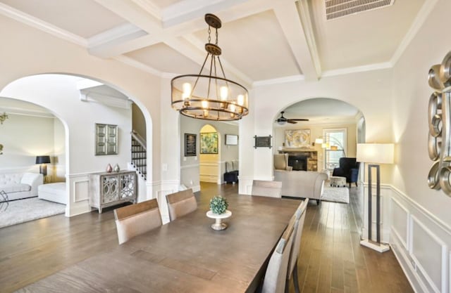 dining area featuring beamed ceiling, ceiling fan with notable chandelier, dark hardwood / wood-style flooring, and a fireplace