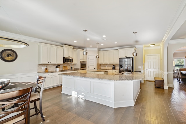 kitchen with an island with sink, decorative light fixtures, appliances with stainless steel finishes, and dark wood-type flooring