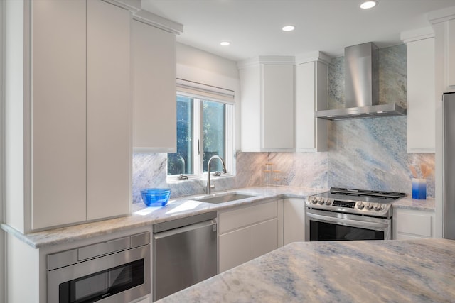 kitchen with wall chimney range hood, white cabinetry, appliances with stainless steel finishes, and a sink