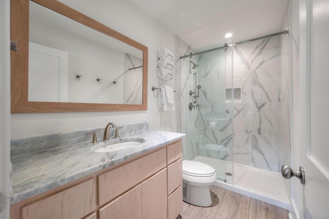 bathroom featuring wood finished floors, toilet, a marble finish shower, and vanity