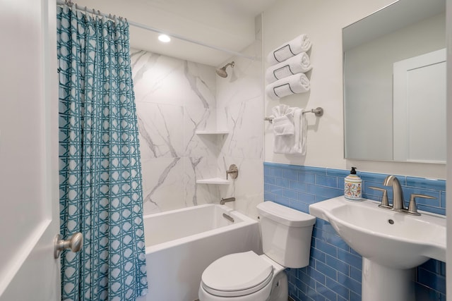 bathroom with wainscoting, a sink, shower / tub combo with curtain, toilet, and tile walls