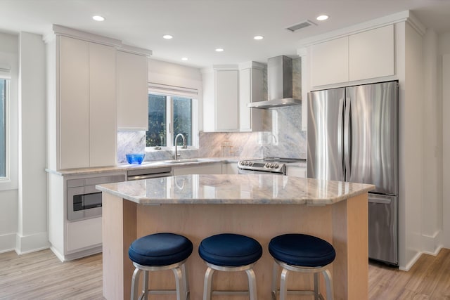 kitchen with a sink, wall chimney exhaust hood, stainless steel appliances, a kitchen bar, and visible vents