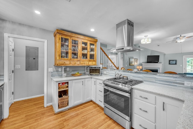 kitchen featuring stainless steel gas range oven, island range hood, white cabinets, and light hardwood / wood-style flooring