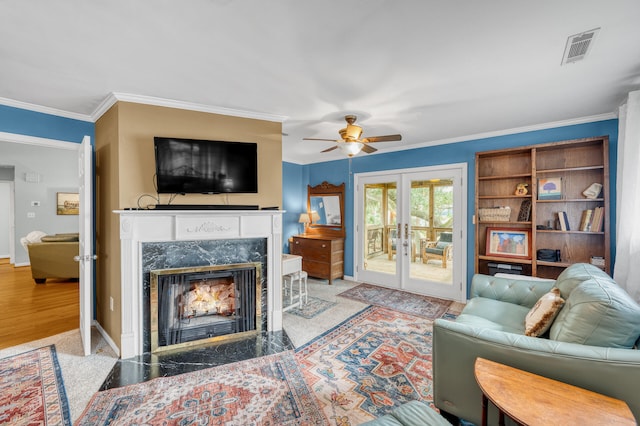 living room with a high end fireplace, french doors, ceiling fan, crown molding, and light hardwood / wood-style flooring