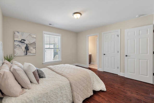 bedroom with dark wood finished floors, visible vents, baseboards, and connected bathroom