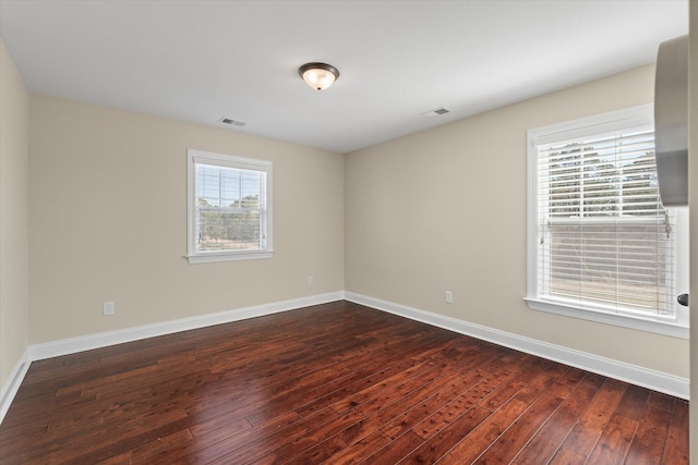 empty room featuring visible vents, baseboards, and dark wood-style floors