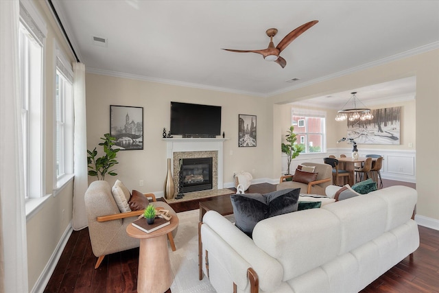 living area with visible vents, a fireplace with flush hearth, ornamental molding, dark wood-type flooring, and ceiling fan with notable chandelier