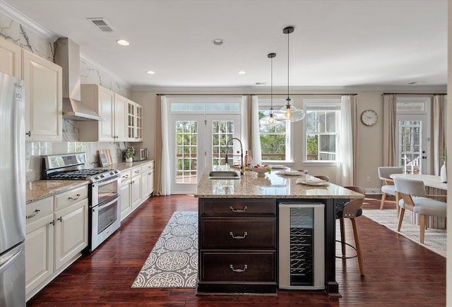 kitchen featuring visible vents, a sink, wine cooler, appliances with stainless steel finishes, and wall chimney range hood