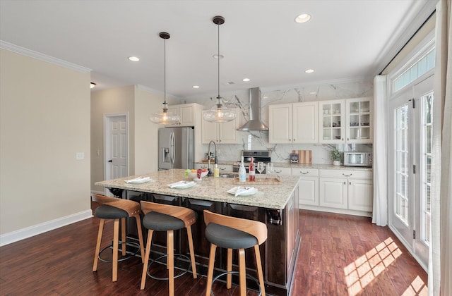 kitchen with dark wood finished floors, a center island with sink, appliances with stainless steel finishes, and wall chimney range hood