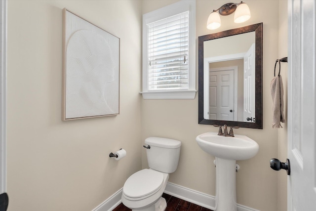 bathroom with toilet, wood finished floors, baseboards, and a sink