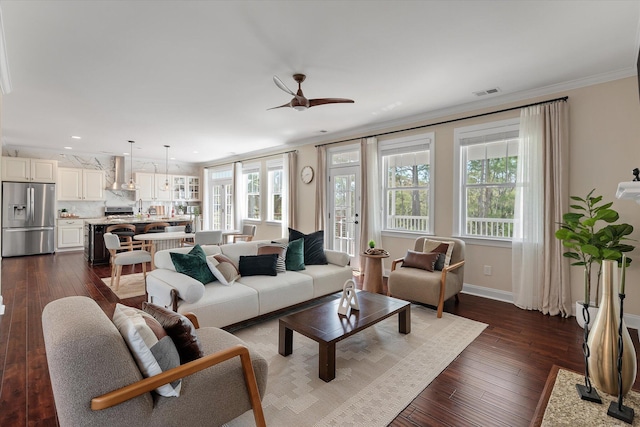 living area with dark wood-style floors, plenty of natural light, and ornamental molding