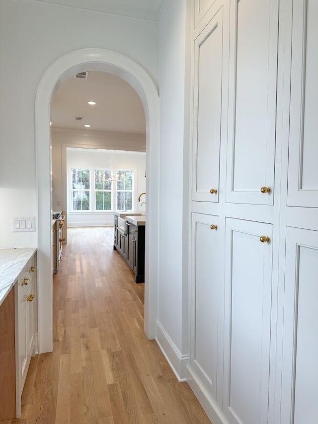 hallway with sink, ornamental molding, and light wood-type flooring