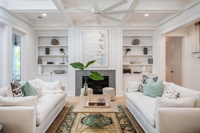 living room with beam ceiling, coffered ceiling, built in features, a high end fireplace, and crown molding