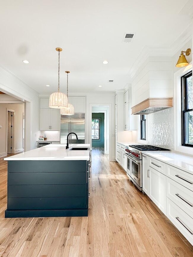 kitchen with white cabinetry, a center island with sink, light hardwood / wood-style floors, and premium appliances