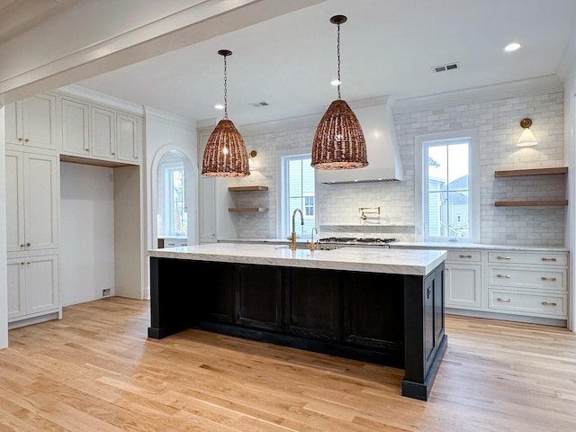 kitchen featuring light hardwood / wood-style flooring, white cabinetry, a kitchen island with sink, and crown molding