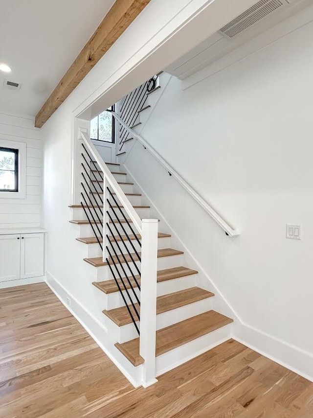 staircase featuring beamed ceiling, hardwood / wood-style flooring, and wooden walls