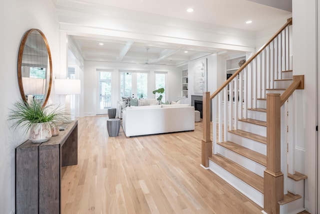 living room with beamed ceiling, built in shelves, light hardwood / wood-style flooring, and coffered ceiling