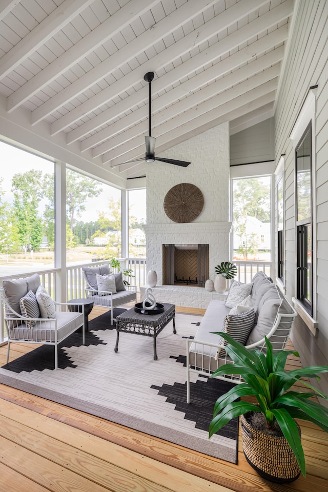 sunroom featuring a fireplace, lofted ceiling with beams, ceiling fan, and a healthy amount of sunlight