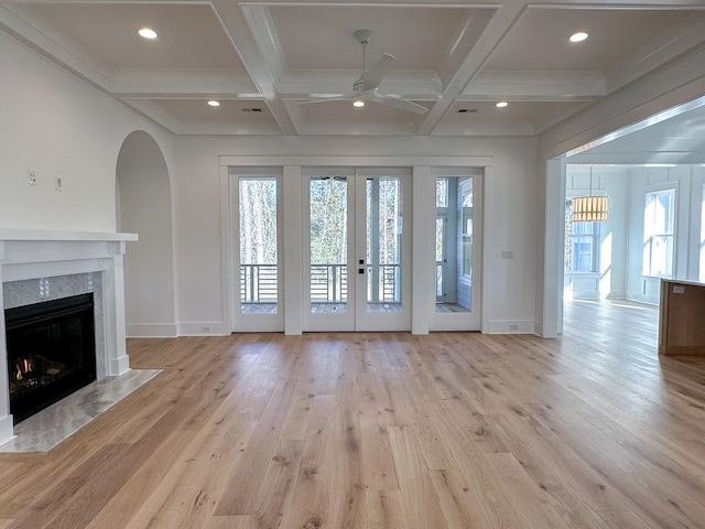 unfurnished living room featuring beam ceiling, light wood-type flooring, coffered ceiling, and a premium fireplace