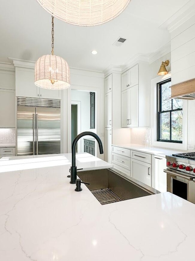 kitchen with light stone countertops, ornamental molding, premium appliances, white cabinets, and hanging light fixtures