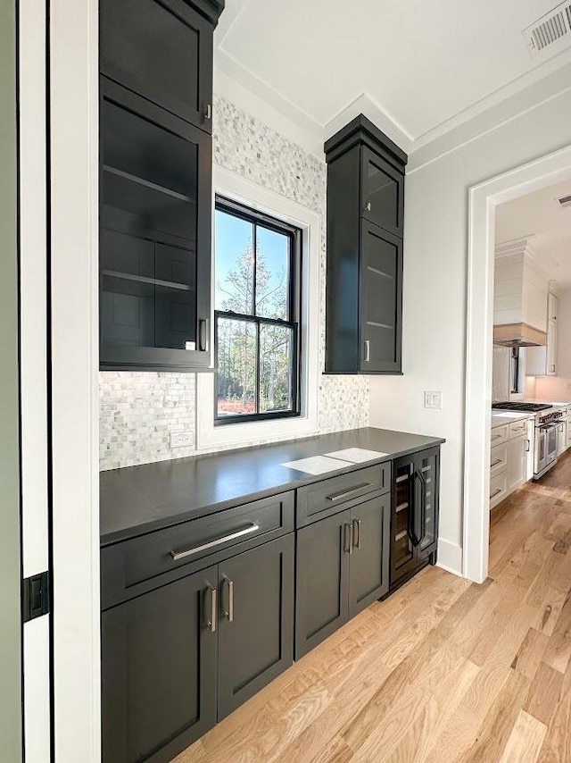 kitchen featuring range with two ovens, crown molding, decorative backsplash, light wood-type flooring, and beverage cooler