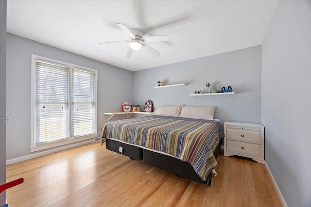 bedroom featuring ceiling fan, baseboards, a textured ceiling, and wood finished floors