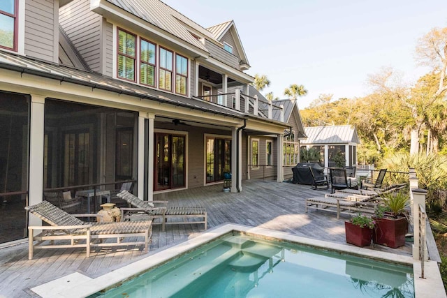 back of property with metal roof, a sunroom, a deck, and a balcony