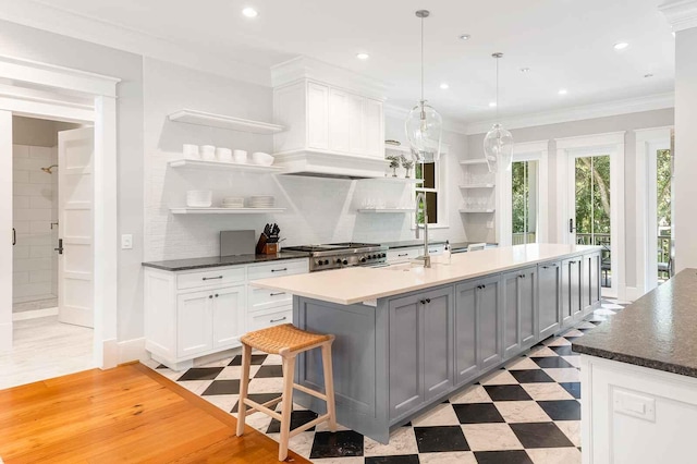 kitchen with decorative backsplash, gray cabinets, open shelves, an island with sink, and light floors