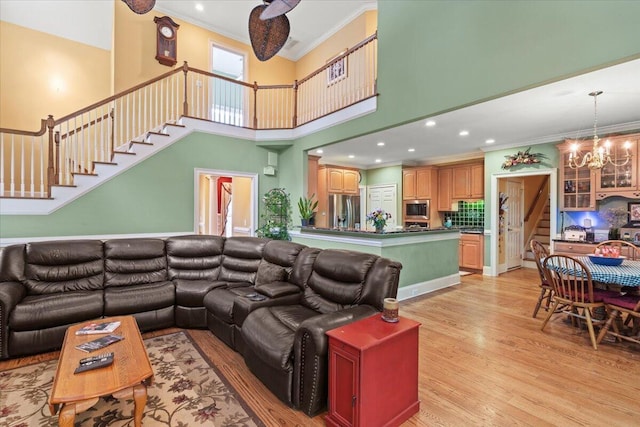 living area featuring crown molding, a chandelier, stairs, light wood finished floors, and a towering ceiling