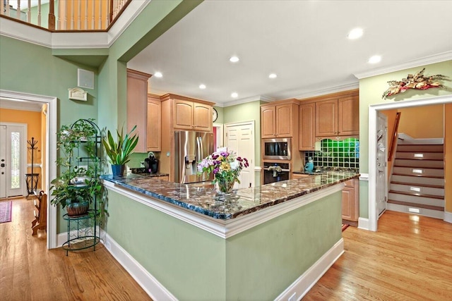 kitchen with appliances with stainless steel finishes, crown molding, dark stone counters, a peninsula, and light wood-type flooring