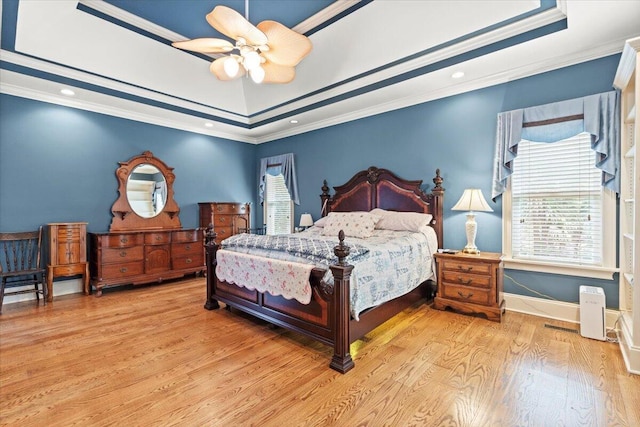 bedroom featuring a raised ceiling, multiple windows, wood finished floors, crown molding, and a ceiling fan