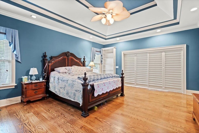 bedroom with wood finished floors, crown molding, a tray ceiling, ceiling fan, and baseboards