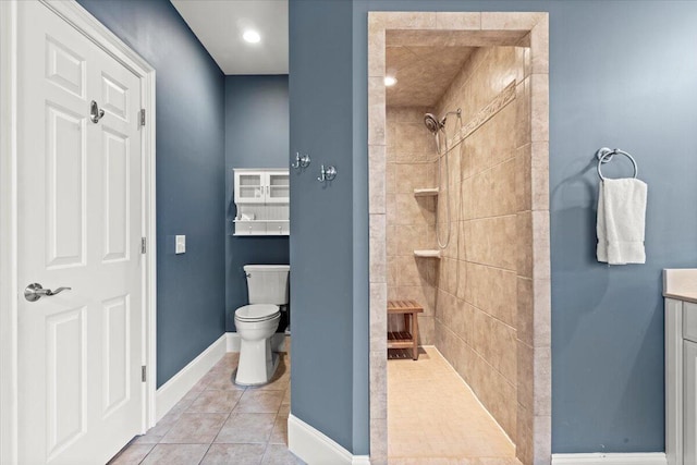 bathroom featuring tiled shower, toilet, tile patterned flooring, vanity, and baseboards