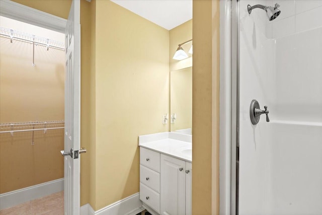 bathroom with a walk in closet, a shower, vanity, baseboards, and tile patterned flooring