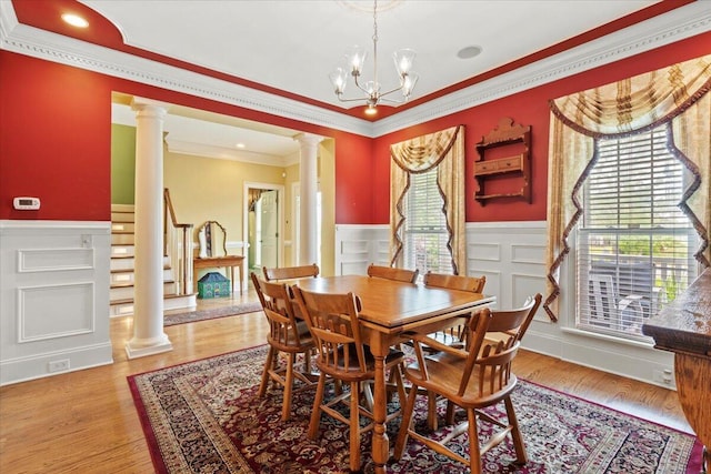 dining room with decorative columns, a wainscoted wall, ornamental molding, a chandelier, and light wood-style flooring