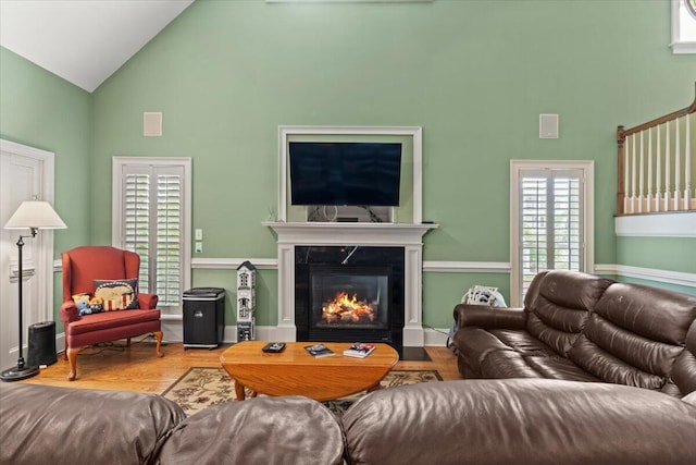 living area with high vaulted ceiling, a glass covered fireplace, and wood finished floors